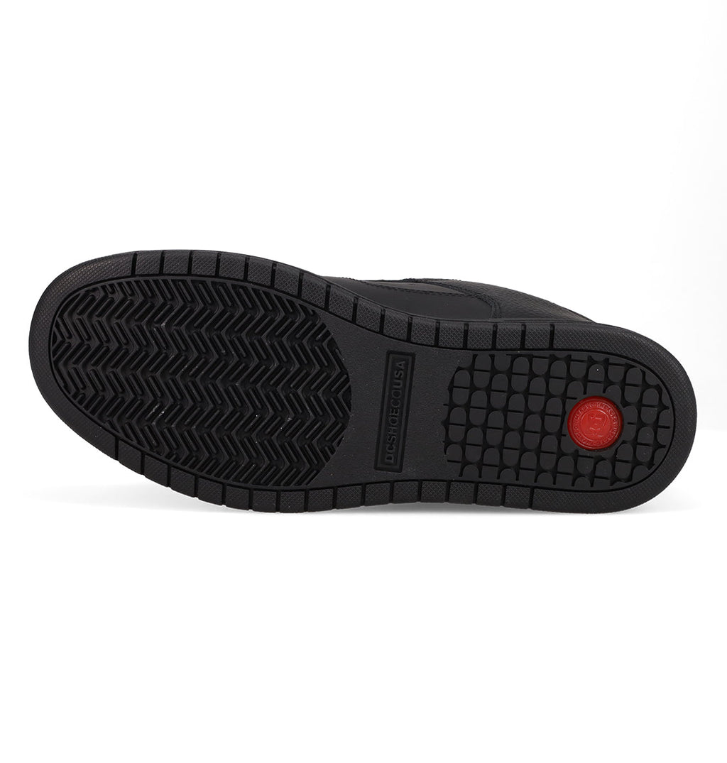 Black rubber sole with patterned tread—zigzag grooves on the left, square grid on the right, and a red circular accent near the heel. The raised central section features “DASHEDCOUSA.” This performance-driven sole design of the Men’s Manteca 4 SE Shoes by DC Shoes pays homage to heritage models like the Manteca SE, offering both style and reliable grip.