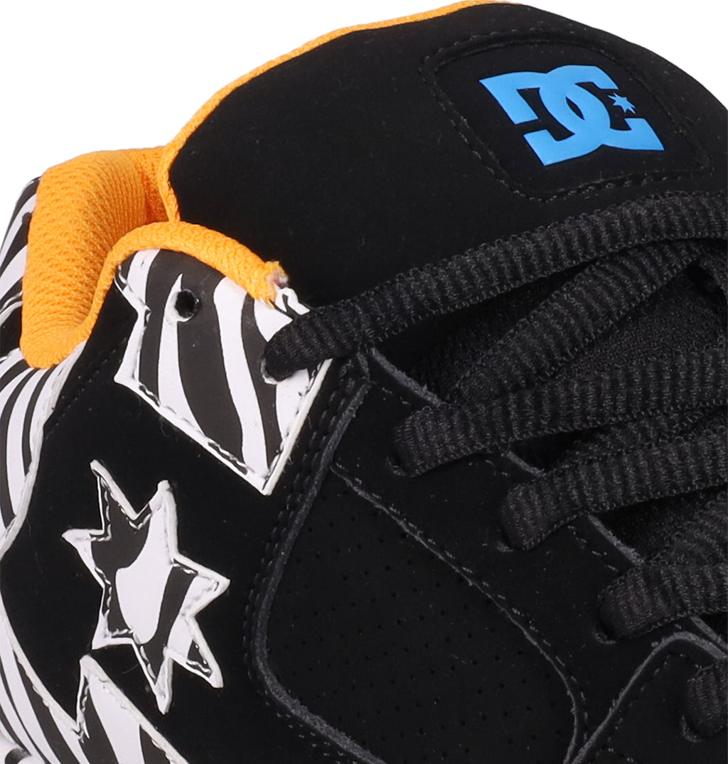 Close-up of Women's DC Command Shoes by DC Shoes—black skate shoes featuring white zebra-patterned stars, yellow lining, black laces, and a blue DC logo on the tongue that highlights their street-inspired style and authentic skate heritage.