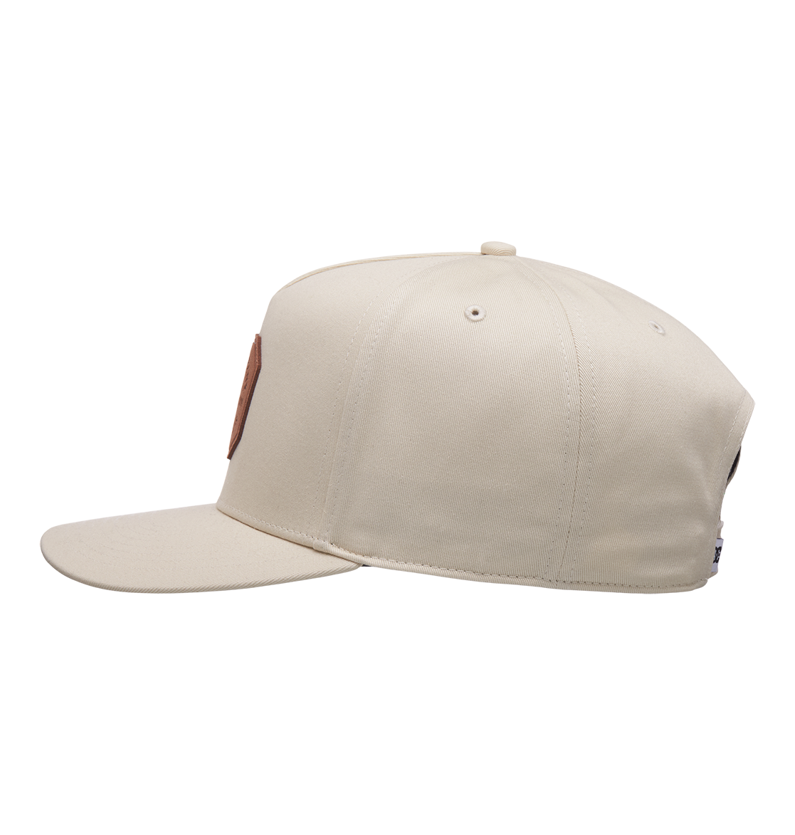 The Men's Reynotts Cap by DC Shoes is displayed side-on against a white background. This beige skate cap features a round brown DC patch on the front and visible stitching along its panels.
