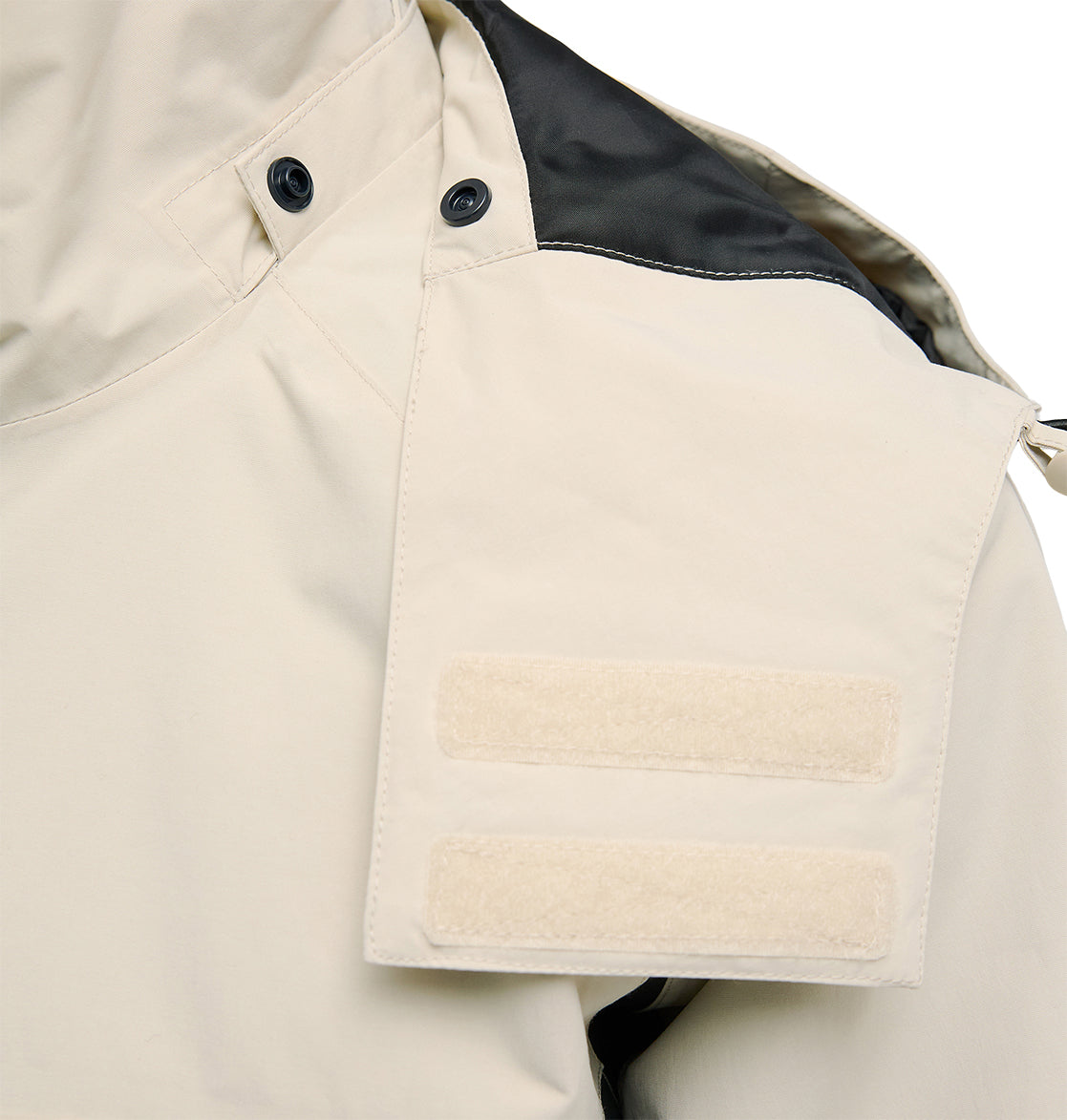 A close-up of the Mountain Lab Jacket 20K by DC Shoes in light beige, showcasing a shoulder epaulet with two horizontal Velcro strips and black buttons. Engineered for optimal snow performance, this jacket features a black accent on the upper shoulder and delivers breathable protection during challenging weather conditions.
