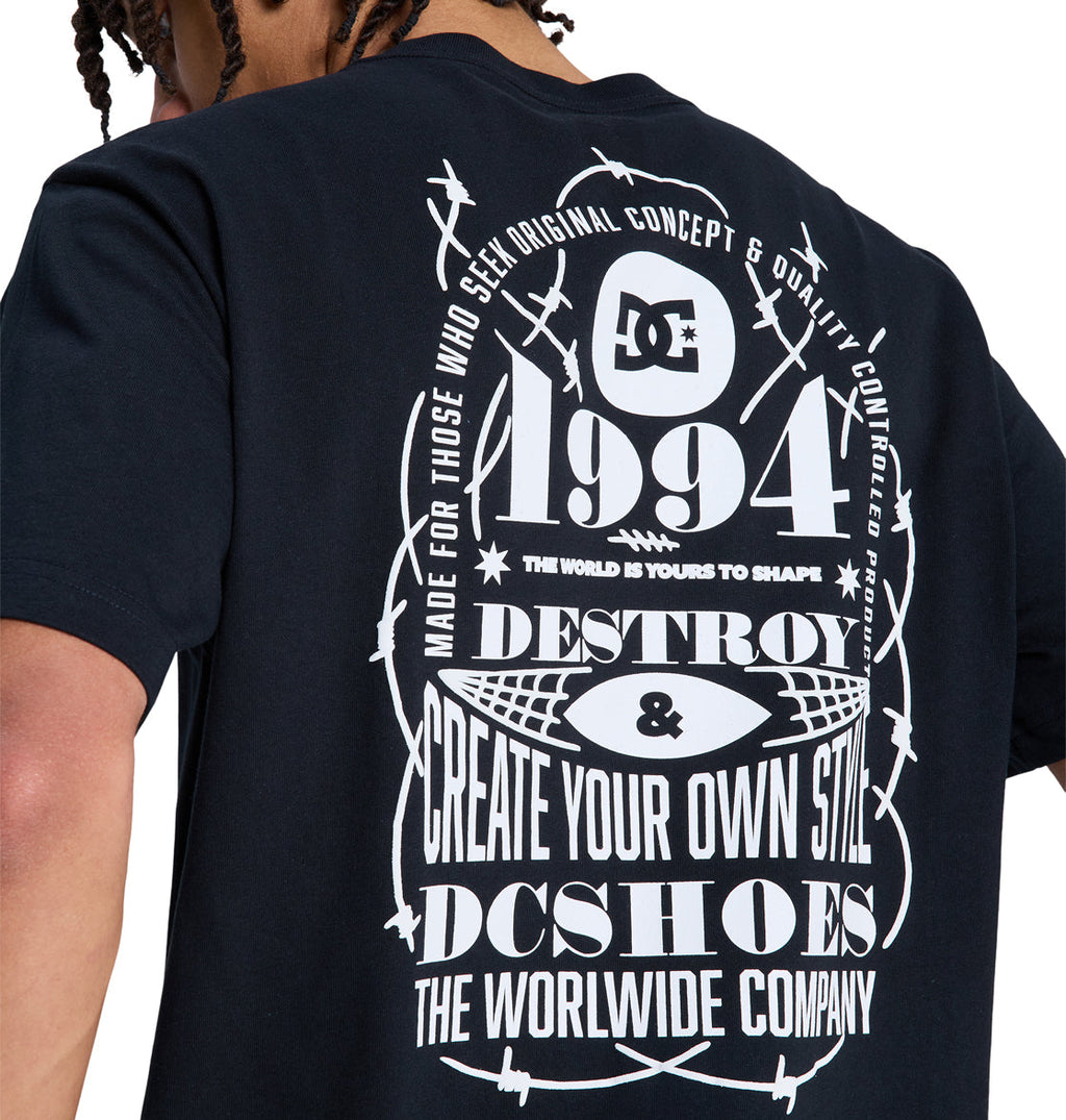 Back view of a person wearing a black Reebok Shape Or Destroy Hss T-shirt with white graphic text and designs, including barbed wire, 1994, Destroy & Create Your Own Style, and The Worldwide Company.